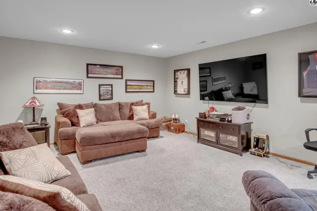Spacious living room with plush brown sectional, large television, and neutral carpet.