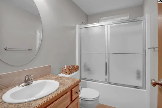 Modern bathroom with a vanity, toilet, and a frosted glass shower/tub combo.