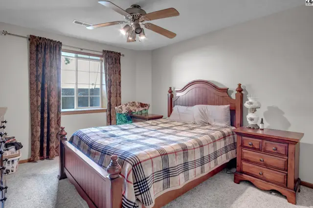 Spacious bedroom with a wooden bed frame, plaid bedding, and a ceiling fan.