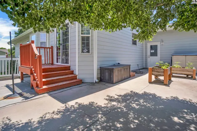 Exterior view of a light gray home with a red wooden deck and concrete patio.