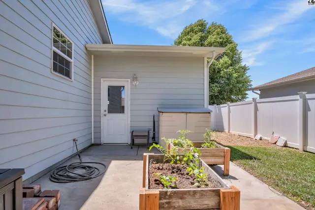 Exterior view of a home with a backyard patio, raised garden beds, and a storage shed.