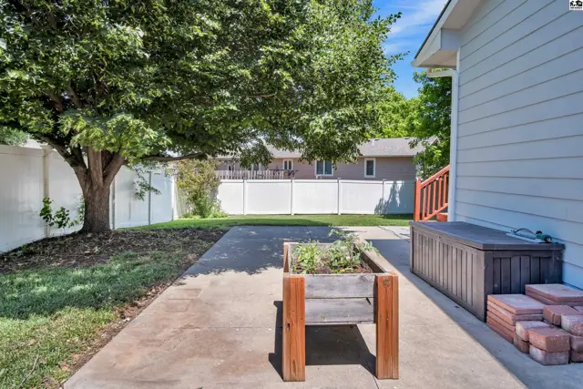 Backyard patio with a wooden planter box, storage bench, and white vinyl fencing.