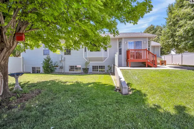 Backyard features a light gray house with a red deck, green lawn, and mature trees.