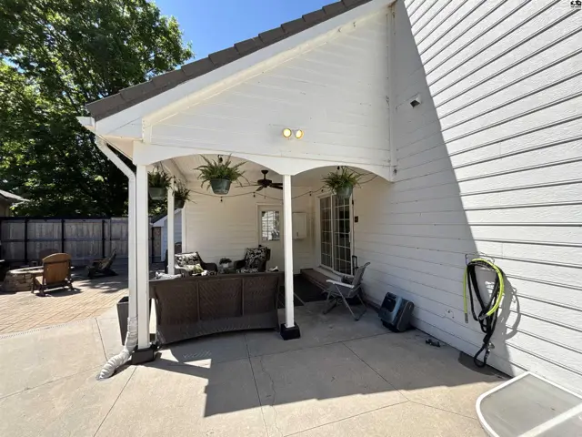 Covered patio with white siding, ceiling fan, and outdoor furniture overlooks a paver patio with a fire pit.