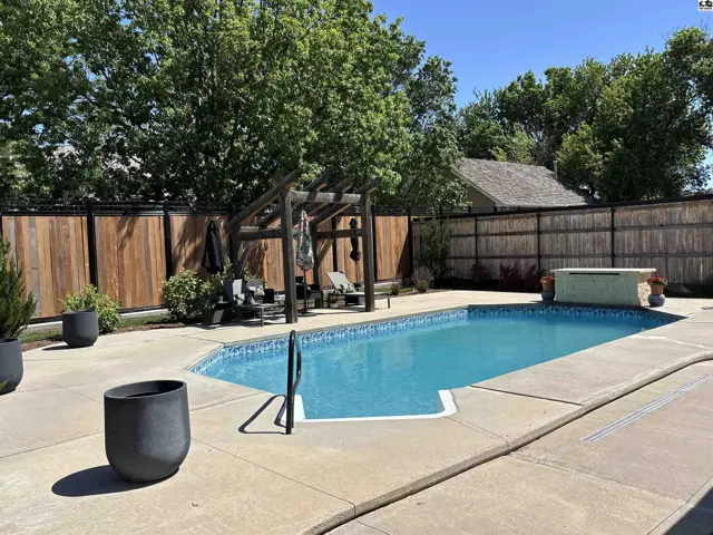 Spacious backyard features a sparkling blue pool, wooden pergola, and privacy fencing.