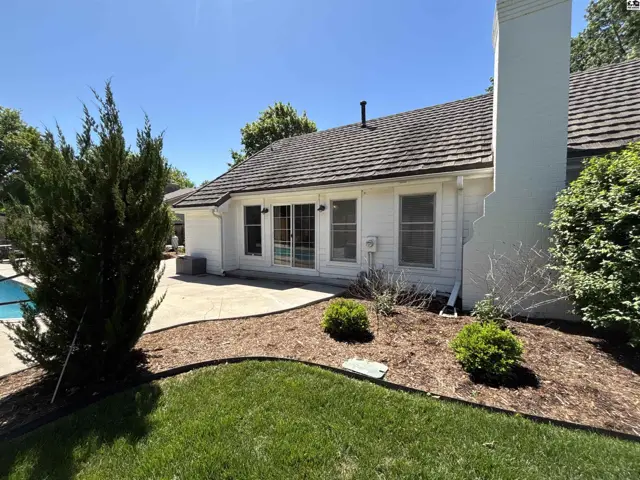 White stucco exterior with a large chimney, patio, and mature landscaping under a clear blue sky.