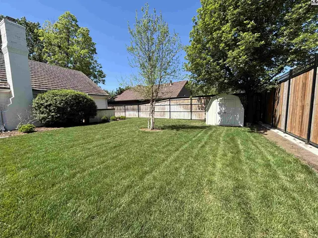Spacious, manicured backyard features a white shed, mature trees, and a wooden privacy fence.