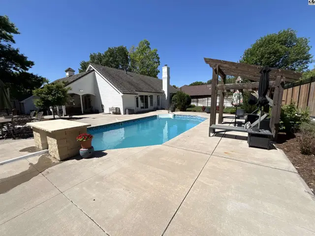 Spacious backyard features a sparkling blue swimming pool, concrete patio, and wooden pergola with seating.