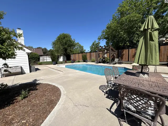 Spacious backyard features a sparkling blue swimming pool, concrete patio, and outdoor dining set.