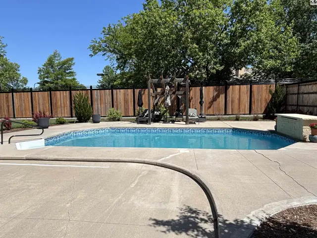 Inground pool with mosaic tile surround, concrete patio, and wooden privacy fence.