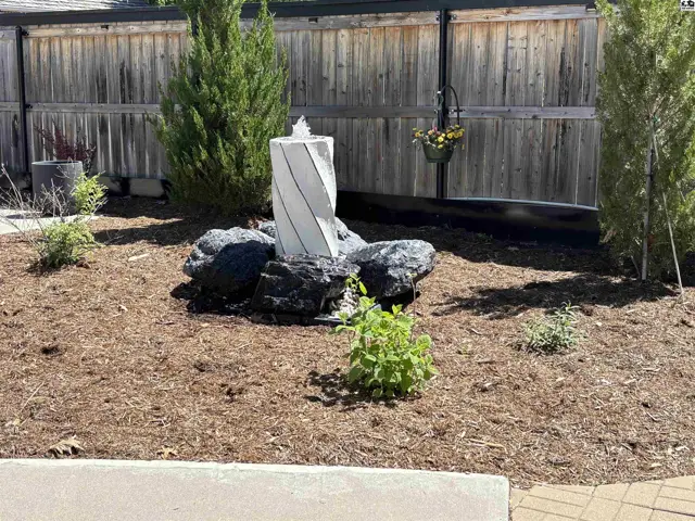 Modern outdoor fountain with white spiral sculpture surrounded by dark rocks and landscaping.