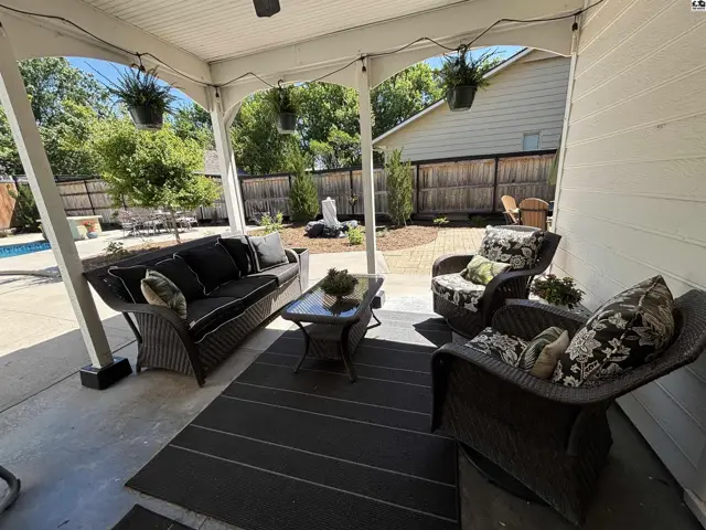 Covered patio with wicker furniture, rug, and string lights overlooks a backyard with a pool and landscaping.