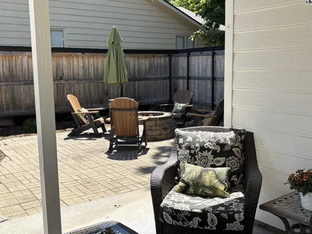 Paved patio with a stone fire pit, Adirondack chairs, and a green umbrella.