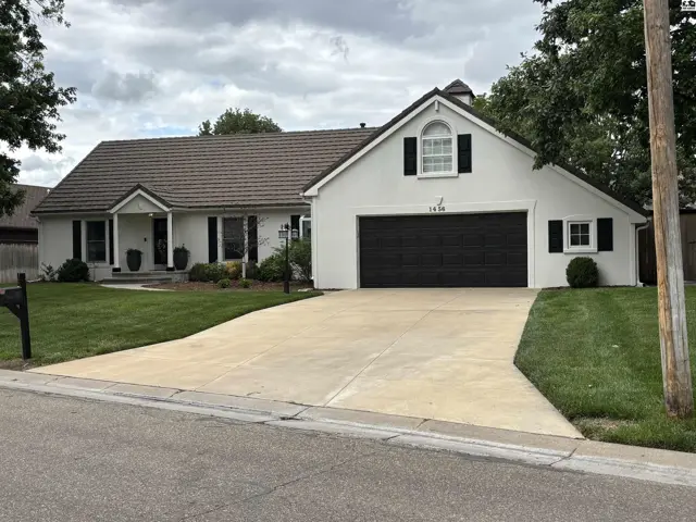 Charming white stucco home with a dark garage door, arched entryway, and manicured lawn.