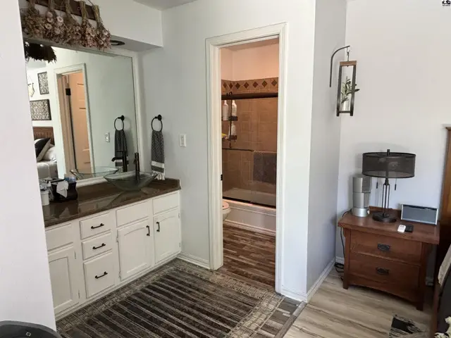 Bright bathroom with white vanity, glass vessel sink, and view into a tiled shower.