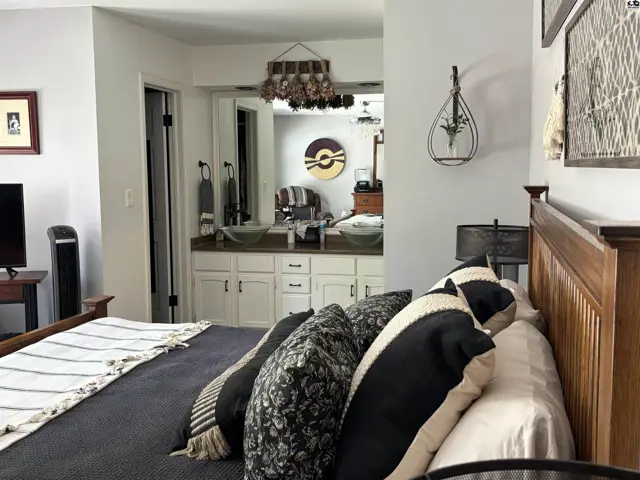 Spacious bedroom with a wooden bed frame, decorative pillows, and a view into a modern bathroom with dual sinks.
