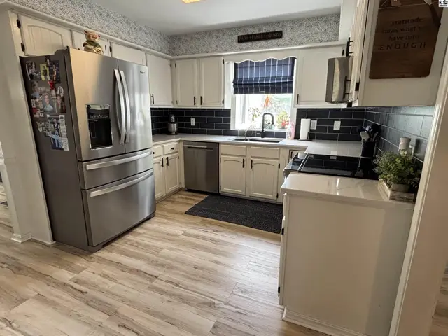 Bright kitchen with white cabinets, stainless steel appliances, dark subway tile backsplash, and wood-look flooring.