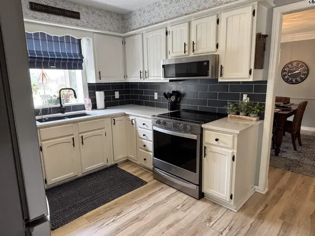 White shaker cabinets, black subway tile backsplash, and stainless steel appliances in a bright kitchen.