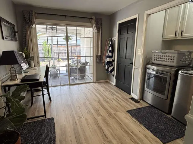 Bright laundry room and home office with light wood floors, stainless steel appliances, and a sliding glass door.