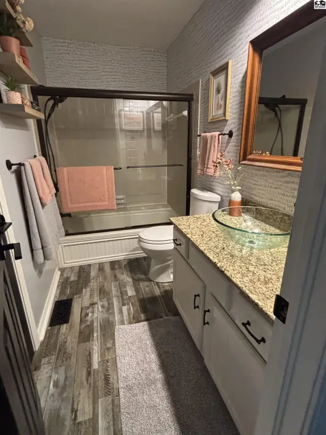 Modern bathroom with wood-look flooring, granite vanity, glass vessel sink, and tiled shower.