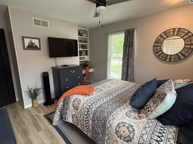 Cozy bedroom with a patterned quilt, dark dresser, built-in shelves, and a decorative mirror.