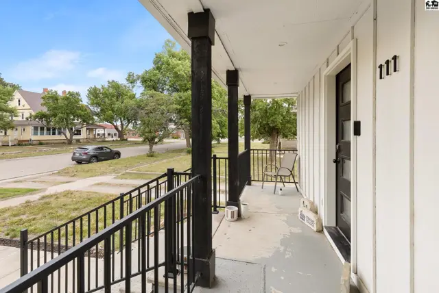 Covered front porch with black railing, white vertical siding, and dark wood columns.