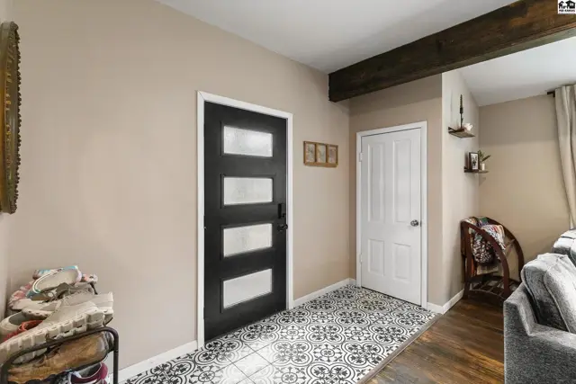 Modern entryway with black paneled door, patterned tile floor, and rustic wood beam.