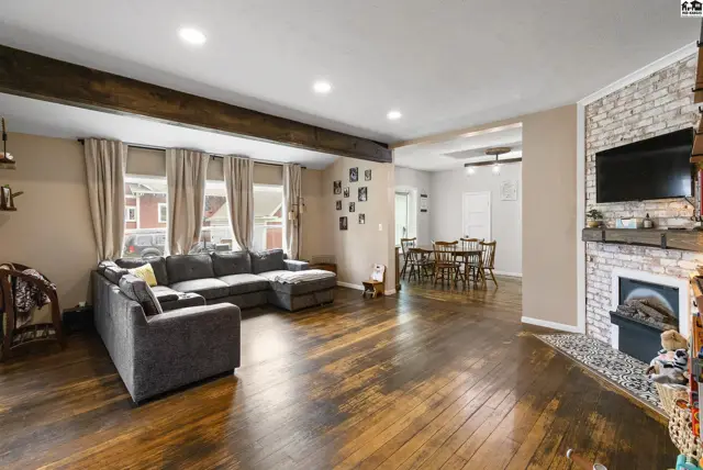 Spacious living room with a large sectional, dark wood floors, exposed beams, and a brick fireplace.