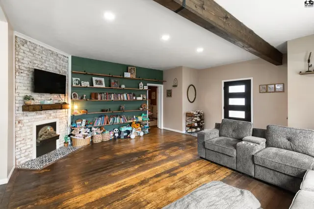 Spacious living room with a white brick fireplace, built-in bookshelves, and exposed wooden ceiling beams.