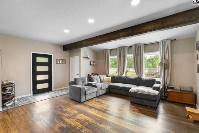 Spacious living room with a large gray sectional, rustic wood beams, and dark-paneled door.