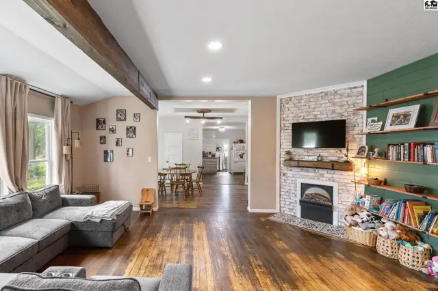Spacious living room with sectional sofa, wood floors, exposed beams, and a brick fireplace with built-in shelving.