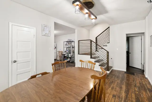 Dining room with wooden table and chairs, featuring dark wood floors and a modern metal-railed staircase.