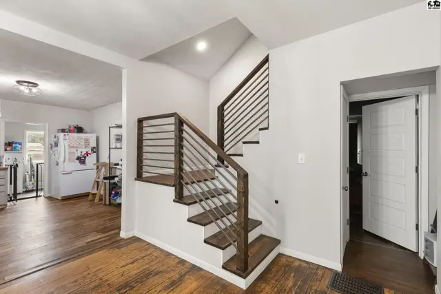 Modern staircase with dark wood treads and metal railing ascends beside a doorway.