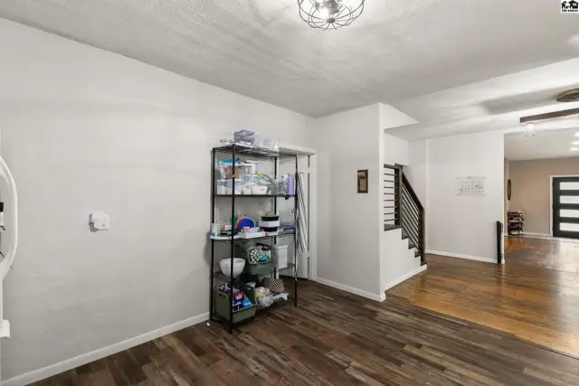 Spacious room with white walls, dark wood floors, and a metal shelving unit near stairs.