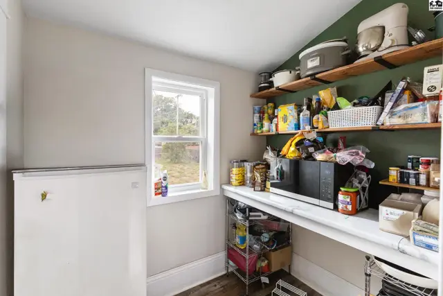 Pantry with white countertops, open shelving, a freezer, and a window overlooking greenery.