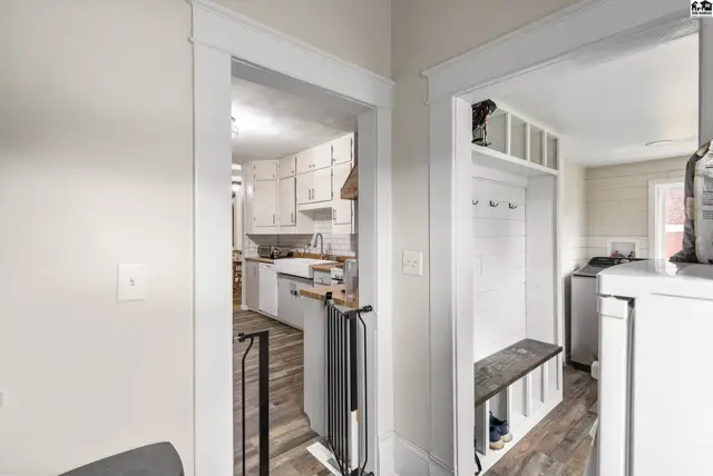 Bright entryway with white built-in storage and a view into a modern kitchen with white cabinets.