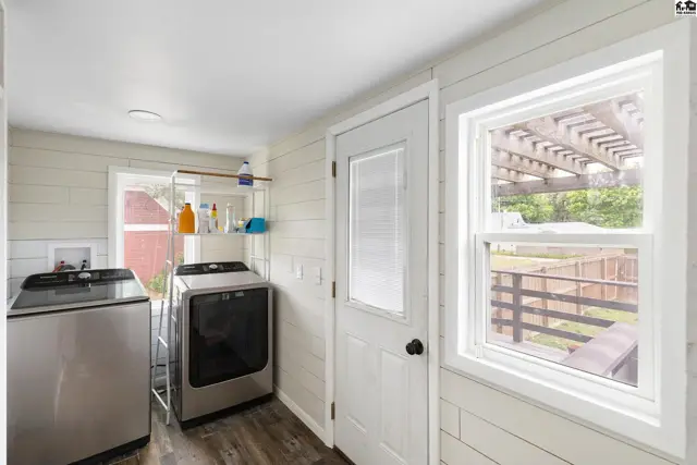 Bright laundry room with stainless steel appliances, shiplap walls, and wood-look flooring.