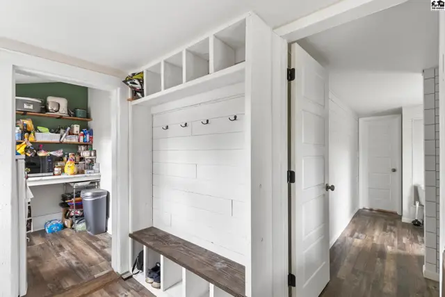 White shiplap mudroom with built-in bench, cubbies, and hooks, adjacent to a pantry.