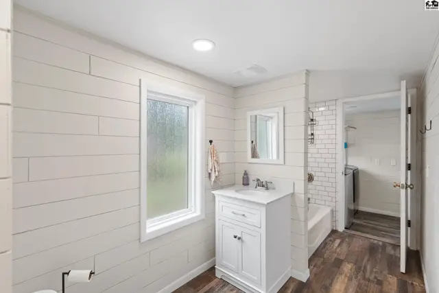 Modern bathroom with shiplap walls, white vanity, and wood-look flooring.