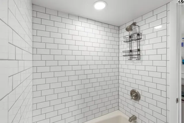Shower stall with white subway tile, brushed nickel fixtures, and a wire caddy.