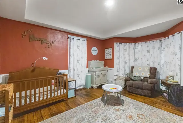 Warm nursery with a wooden crib, changing table, recliner, and patterned curtains.