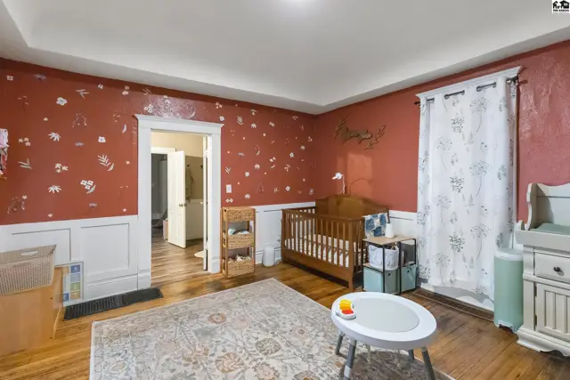Nursery with red floral wallpaper, white wainscoting, wooden crib, and patterned rug.
