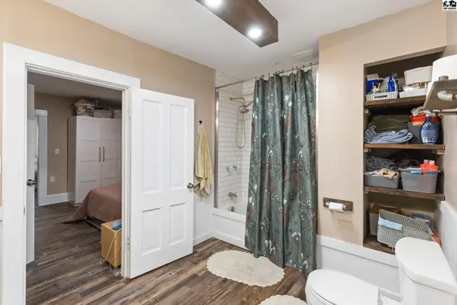 Modern bathroom with wood-look flooring, white subway tile shower, and open shelving.