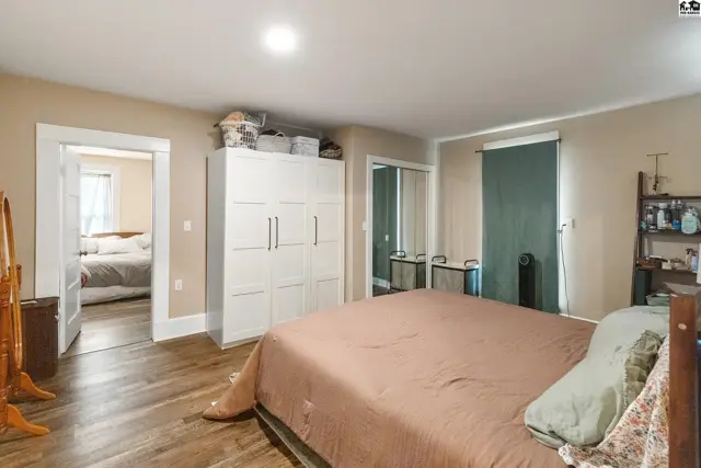 Spacious bedroom with wood floors, large white wardrobe, and an adjoining room with a bed.