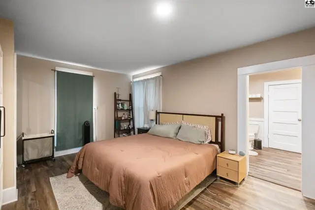 Spacious bedroom with a king-size bed, wood-look flooring, and an open doorway to a bathroom.