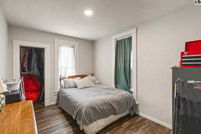 Bedroom with a queen bed, wood-look flooring, and a closet with hanging clothes.