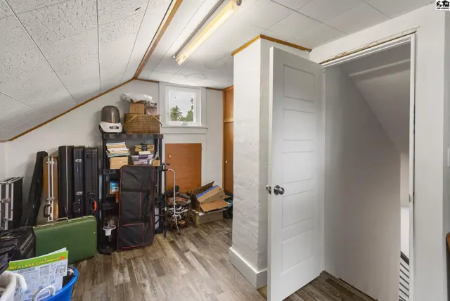 Attic room with wood-look flooring, storage shelves, and a white paneled door.