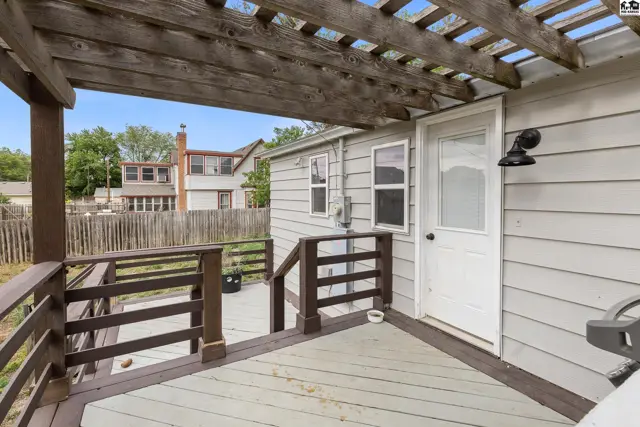Wooden deck and pergola overlook a backyard with a light gray sided house and white door.