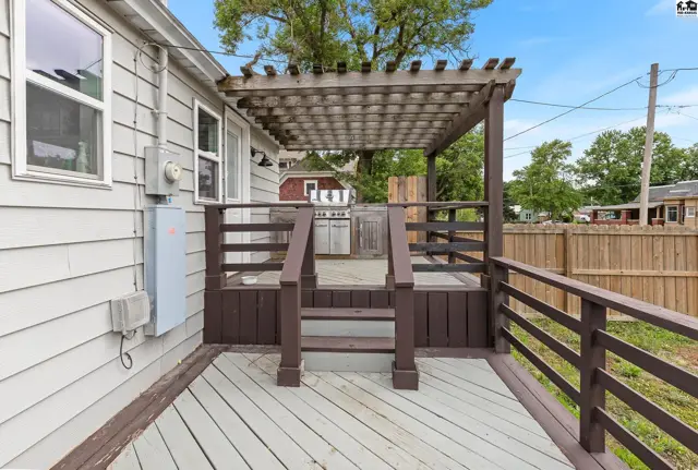 Wooden deck with a pergola and railing, featuring a grill and siding.
