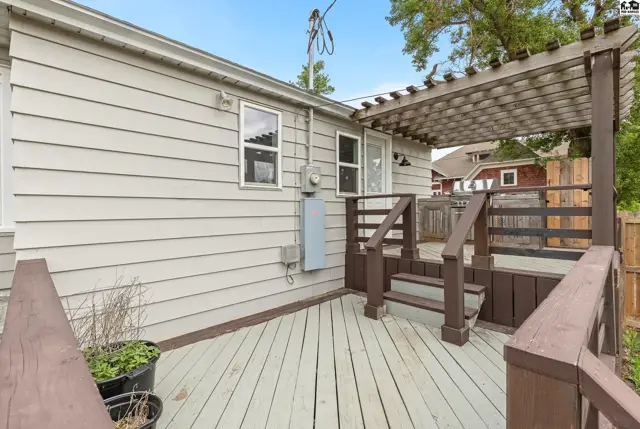 Light-colored wooden deck with dark brown railings and a pergola extends from a light gray sided house.